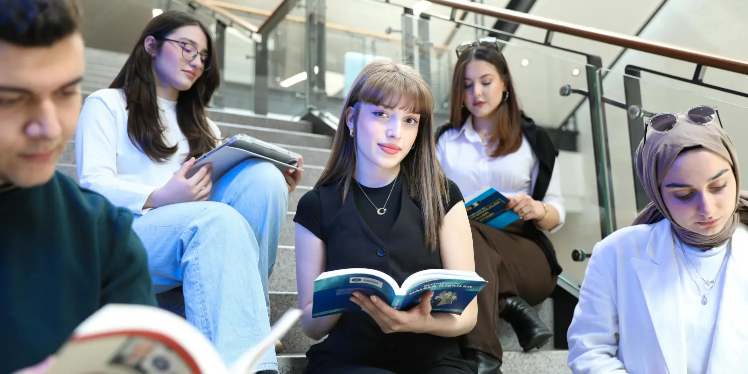 Elinde kitap tutan merdivende oturmuş öğrenciler